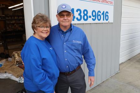 The owners of Powers and Gregory standing in front of their sign wearing blue Powers and Gregory merch.