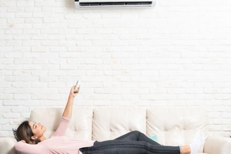 Woman laying on a white couch underneath a mini split unit. 